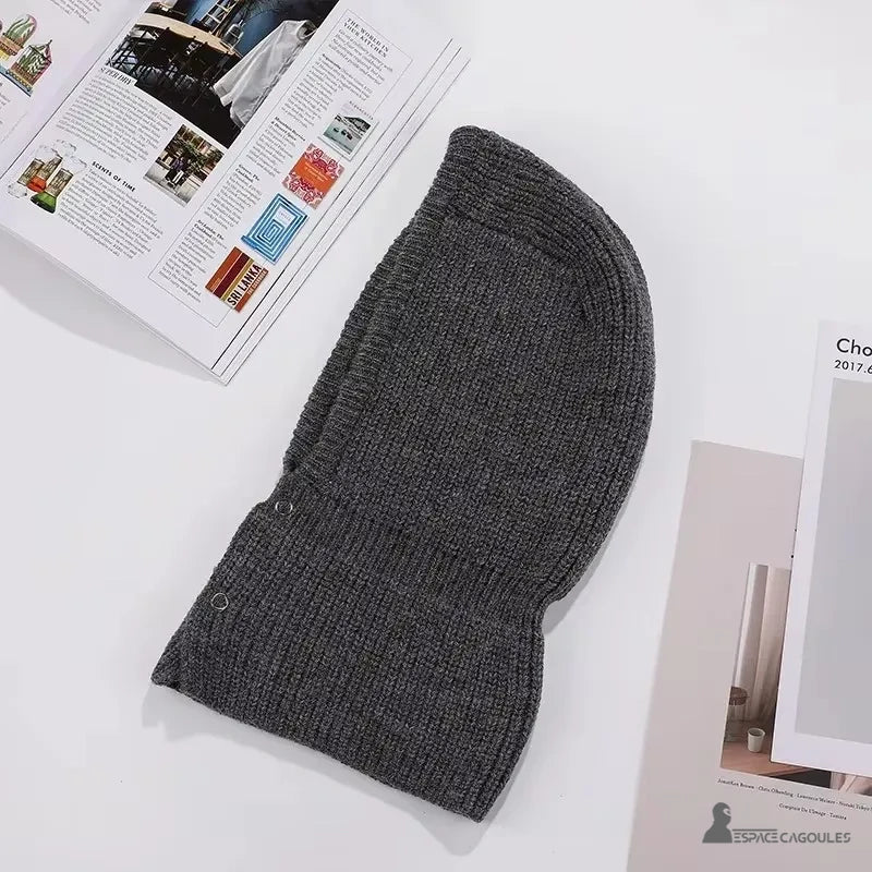 Balaclava Cagoule Tricot gris foncé vue à plat sur une surface blanche avec des magazines ouverts autour