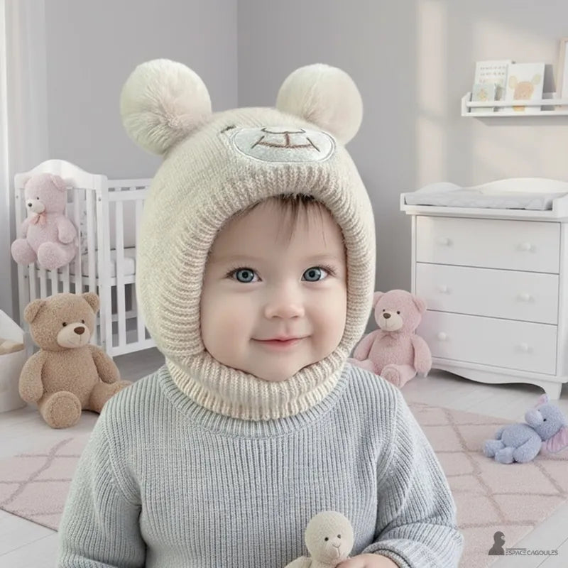 Bonnet Cagoule bébé porté par un nourrisson souriant dans une chambre avec peluches, bonnet tricoté avec oreilles d’ours, Espace Cagoules