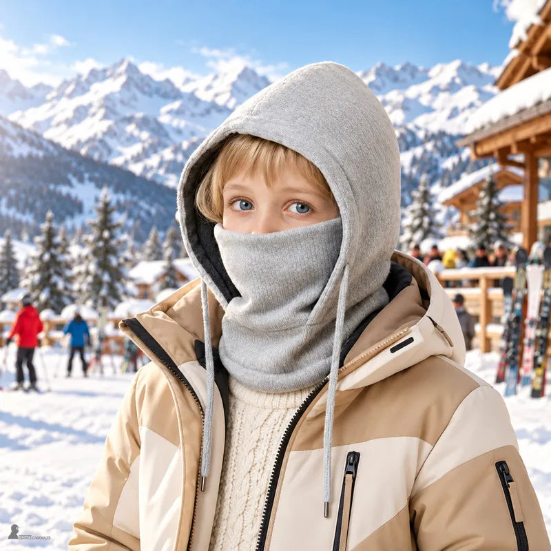 Garçon en bonnet cagoule enfant gris, masque remonté sur le nez, au pied des pistes d'une station de ski - Espace Cagoules