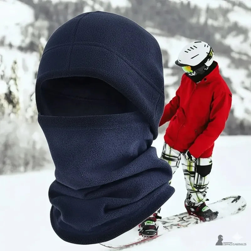 Bonnet cagoule navy porté en montagne, fond enneigé avec un snowboarder en arrière-plan, accessoire chaud pour sports d’hiver Espace Cagoules
