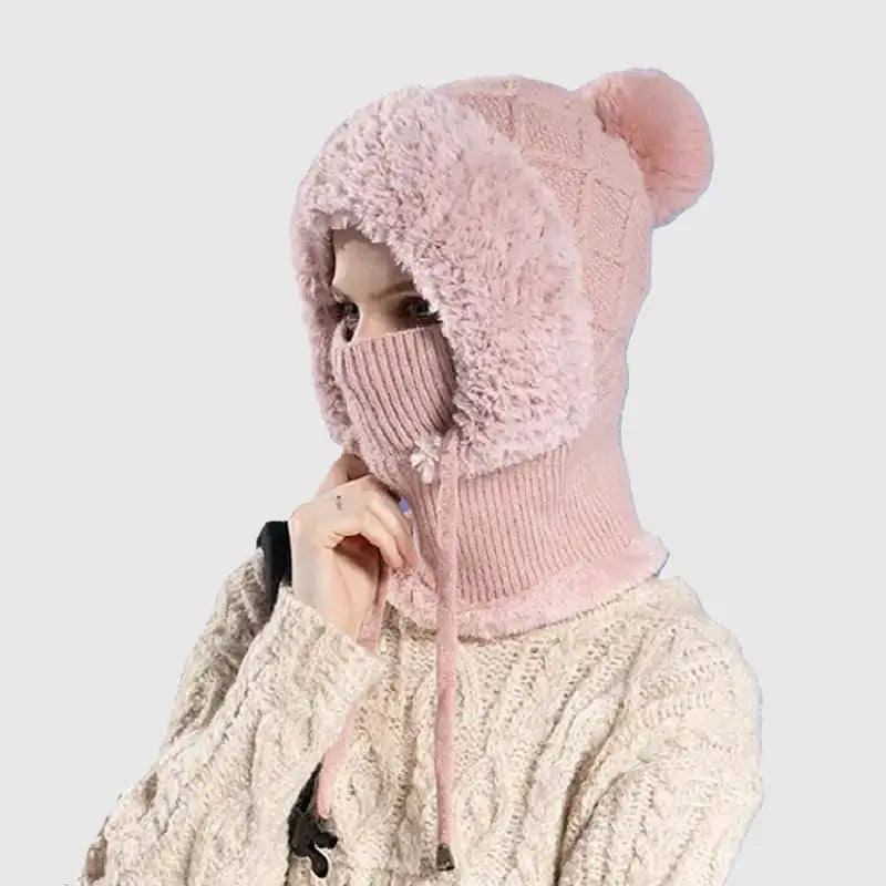 Femme portant un bonnet cagoule tricot rose avec pompon et doublure en fausse fourrure, idéal pour se protéger du froid en hiver.