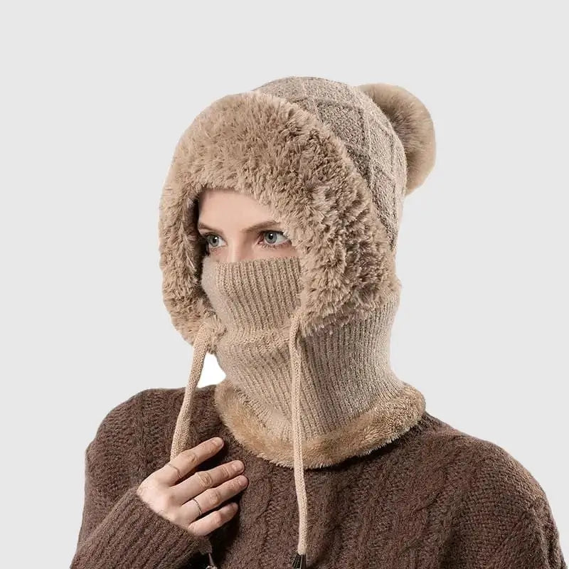 Femme portant un bonnet cagoule tricot kaki avec pompon et doublure en fausse fourrure, idéal pour se protéger du froid en hiver.