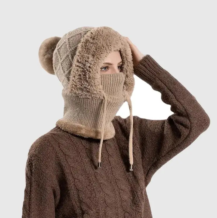Femme portant un bonnet cagoule tricot kaki avec pompon et doublure en fausse fourrure, offrant chaleur et protection pour l'hiver.