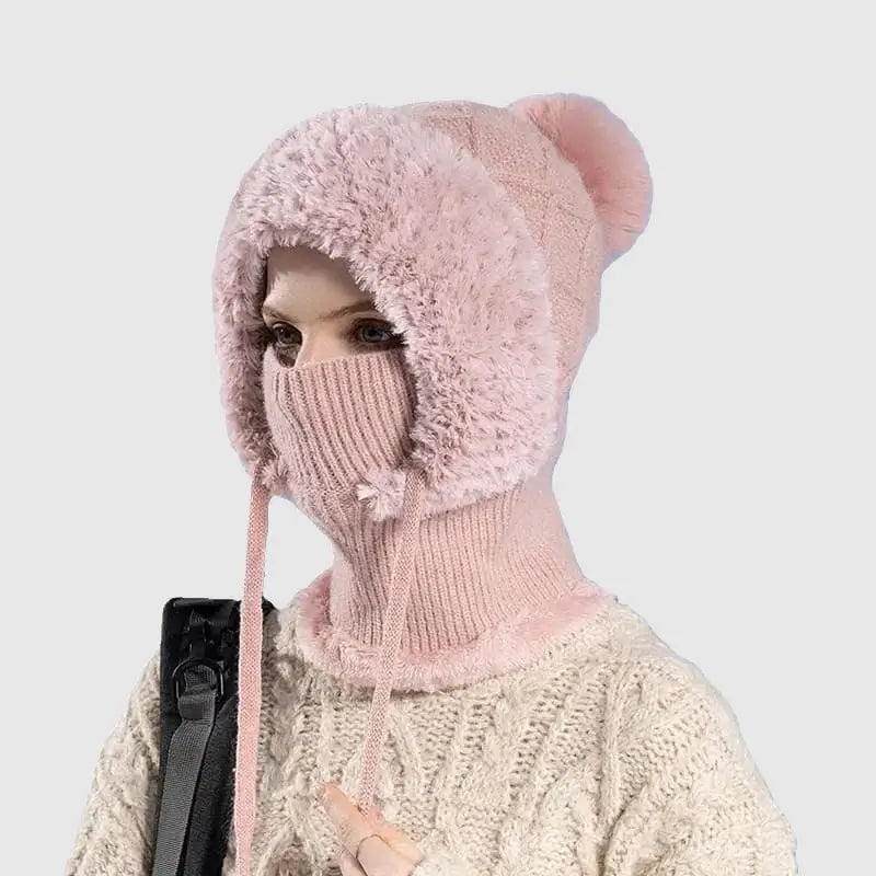 Femme portant un bonnet cagoule tricot rose avec pompon et doublure en fausse fourrure, offrant chaleur et protection pour l'hiver.