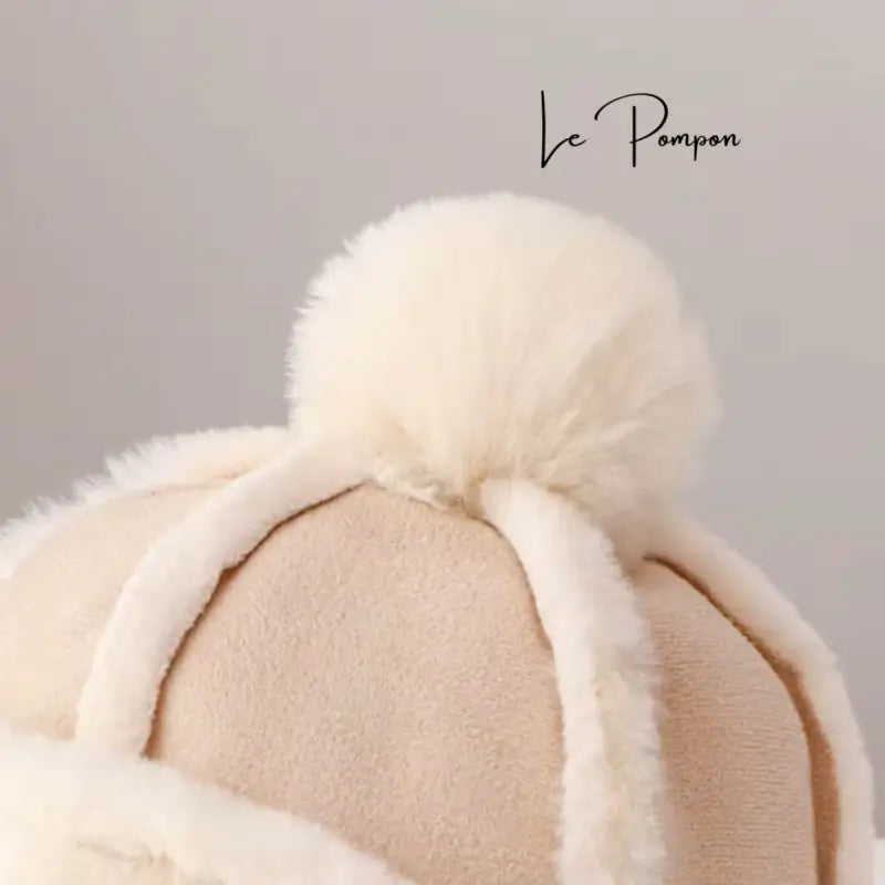 Close-up of the pompom of a beige and white Children's Chapka Hat, highlighting the soft and fluffy texture of the winter accessory.