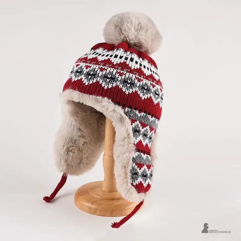 Roter Hut mit schwarz-weißen Mustern, Pompon und beigem Kunstpelz im Inneren, präsentiert auf einer Holzstütze