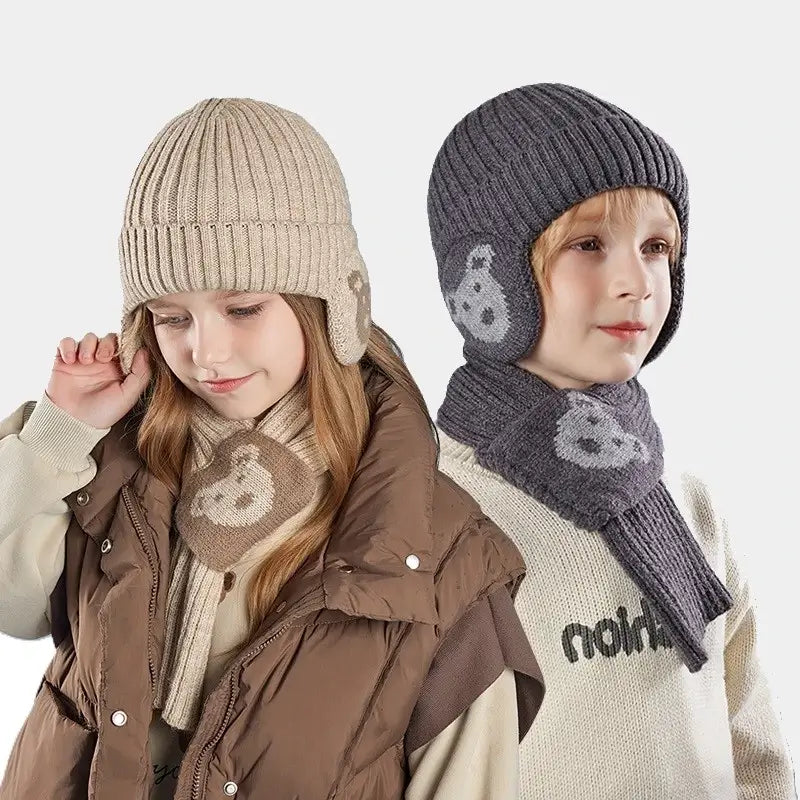 Deux enfants portant un ensemble bonnet Ă©charpe enfant en tricot, avec des motifs d'ours sur les oreilles et l'Ă©charpe. Le garçon, vĂȘtu d'un bonnet et Ă©charpe gris foncĂ©, porte un pull beige, tandis que la fille porte un ensemble beige et une veste matelassĂ©e marron, posant sur un fond neutre.