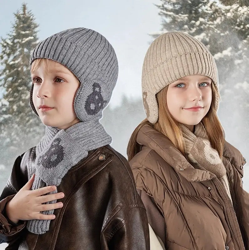 Deux enfants portant un ensemble bonnet écharpe enfant en tricot, avec des motifs d'ours sur les oreilles et l'écharpe, dans un cadre hivernal enneigé. Le garçon porte un ensemble gris et une veste en cuir marron, tandis que la fille porte un ensemble beige avec une veste matelassée marron.