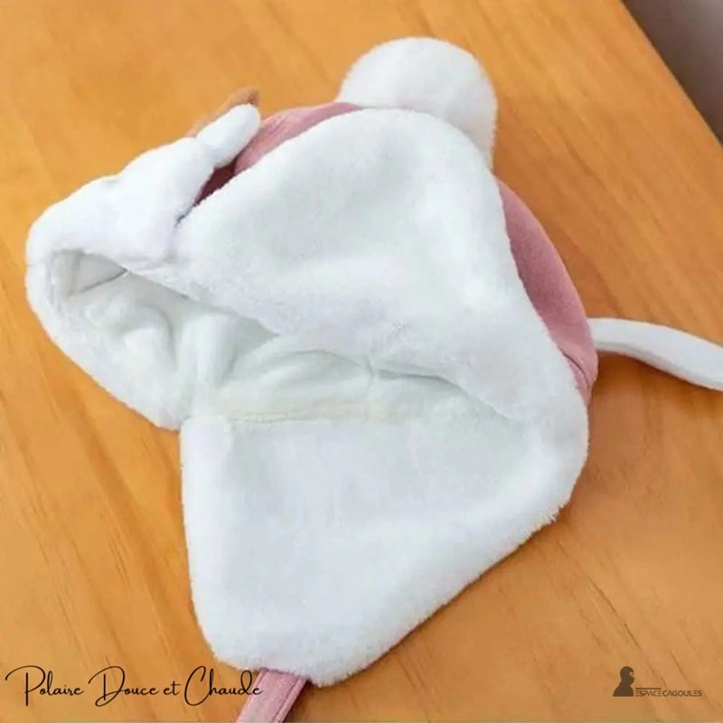 Pink fleece children's hat with white interior, placed on a wooden table in warm interior