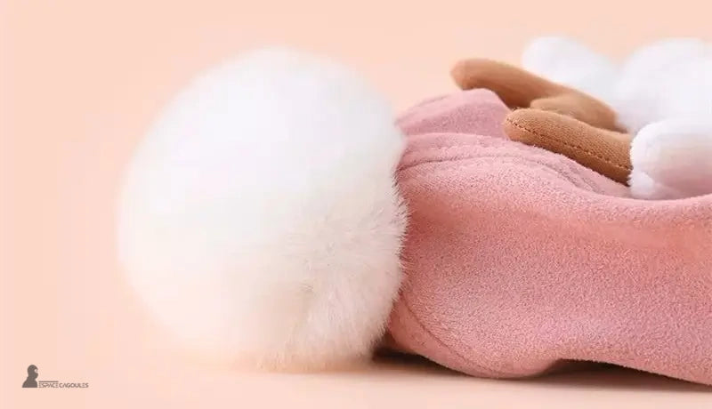 Pink fleece reindeer children's hat with large white pompom seen up close, soft and cozy atmosphere