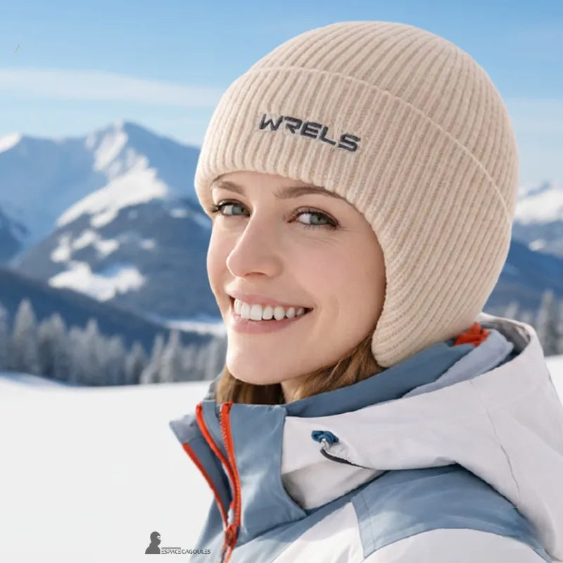 Bonnet sous casque ski beige en maille tricotée douce porté par une femme, forme enveloppante avec cache-oreilles, vue portée en environnement montagne hivernal - Espace Cagoules