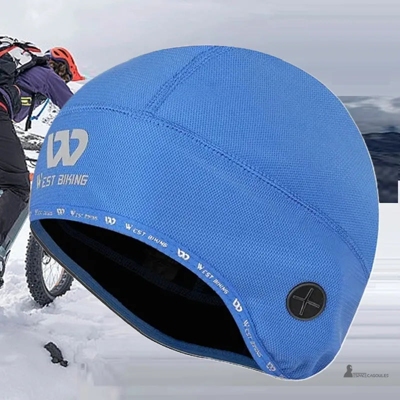 Bonnet sous casque velo bleu West Biking posé sur neige avec cycliste en arriÚre-plan