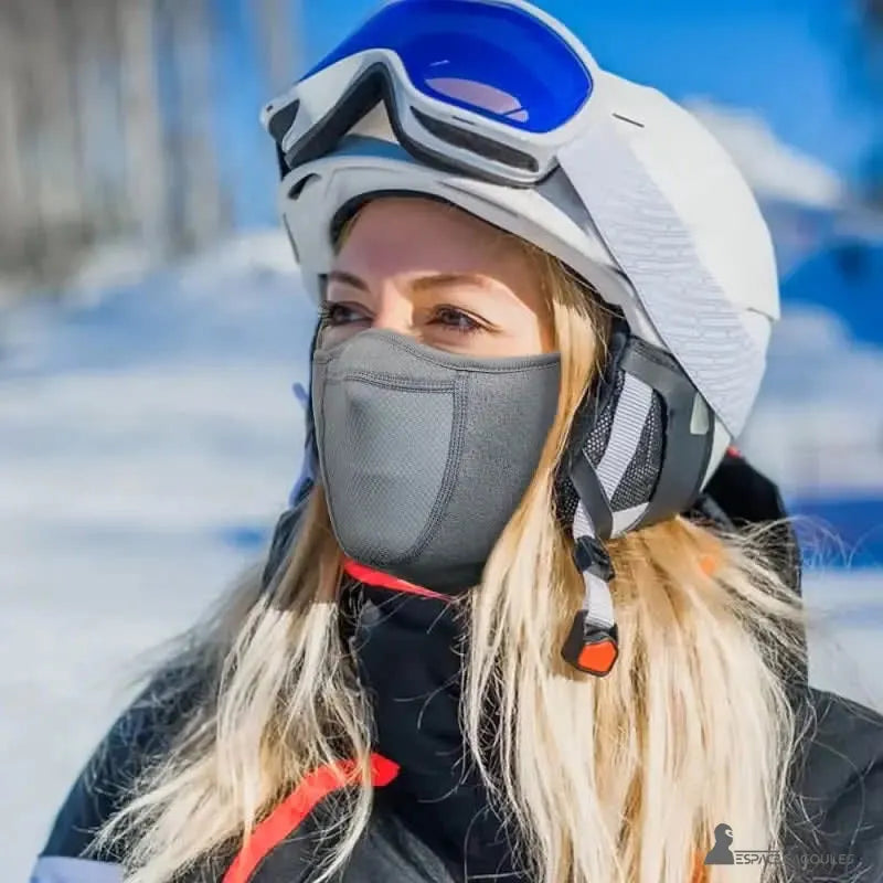 Cache cou cagoule femme grise portée par une skieuse avec casque et masque de ski en montagne