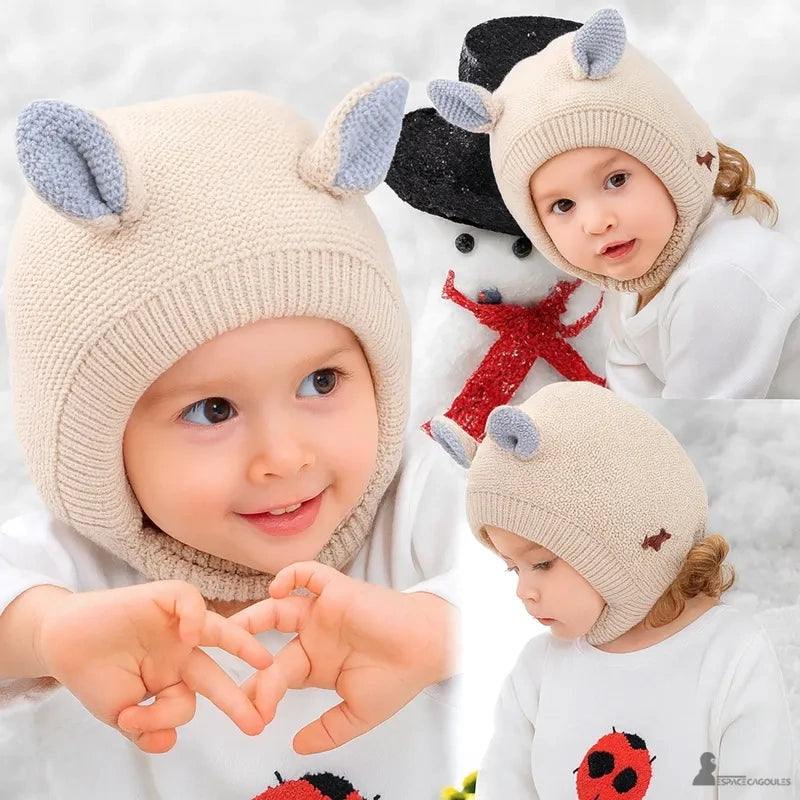 Cagoule Bébé 6 à 36 mois en laine tricotée beige avec oreilles grises, portée par enfant souriant dans un environnement enneigé avec bonhomme de neige en arrière-plan