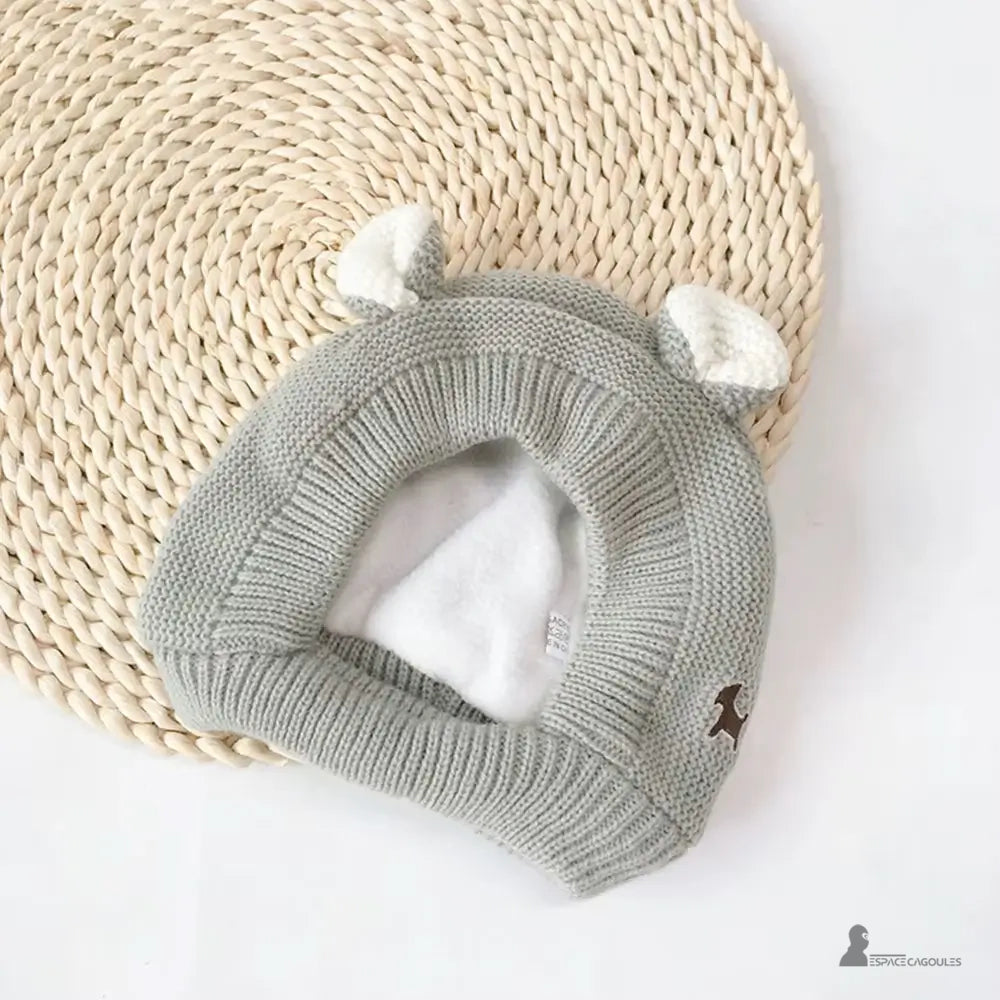 Cagoule Bébé 6 à 36 mois tricot gris avec oreilles blanches, posée à plat sur un tapis tressé rond, doublure polaire blanche visible à l’intérieur
