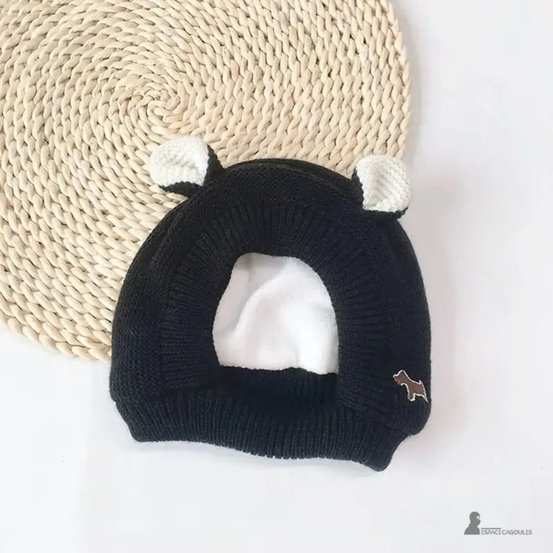 Cagoule Bébé 6 à 36 mois tricot noir avec oreilles blanches et broderie chien marron, posée à plat sur tapis rond en fibres tressées