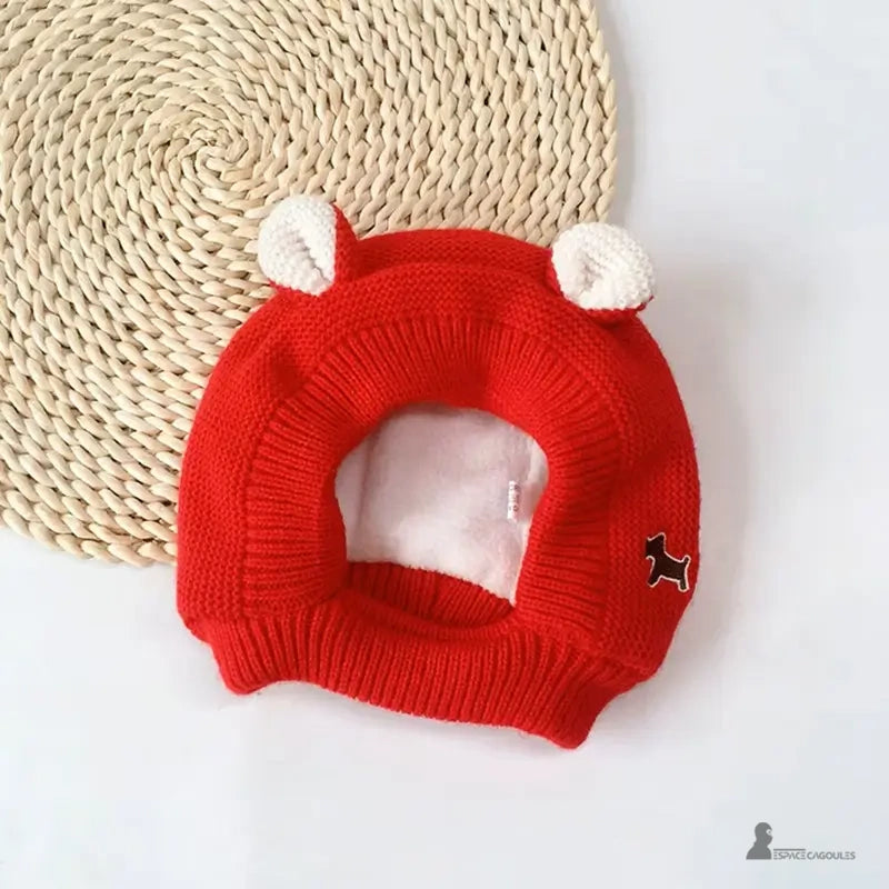 Cagoule Bébé 6 à 36 mois tricot rouge vif avec oreilles blanches et broderie chien marron, posée à plat sur tapis rond tressé clair