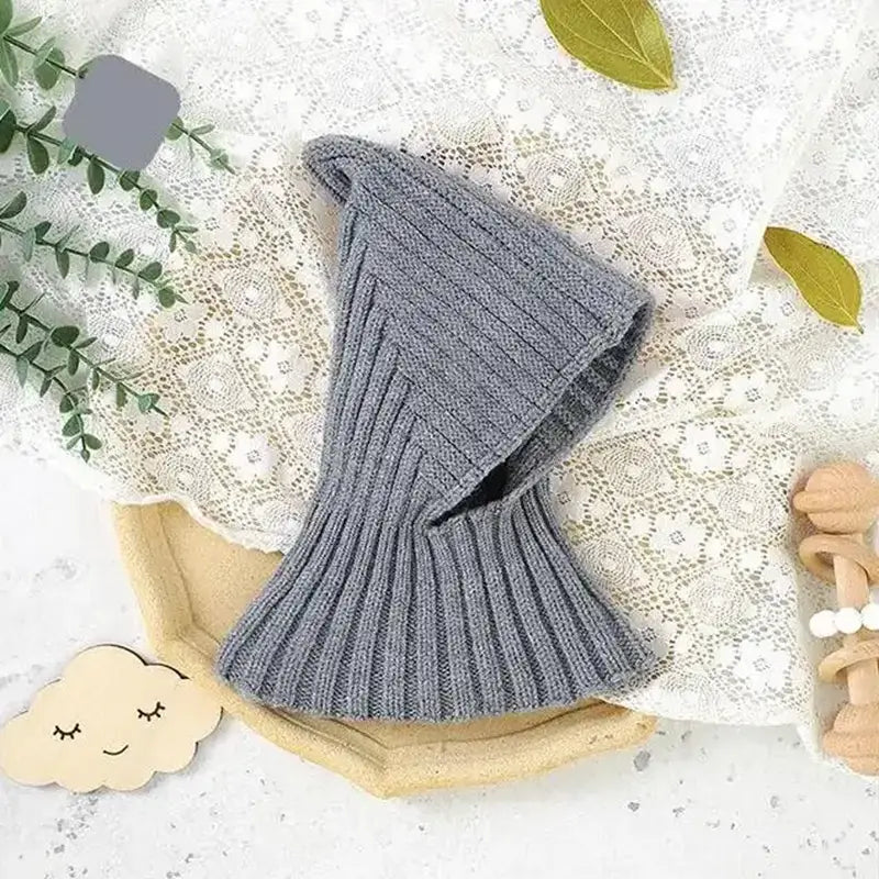 Graue Strick-Sturmhaube für Babys, platziert in einer natürlichen Umgebung, perfekt für den Winter, vereint Wärme und Komfort für aktive Babys.