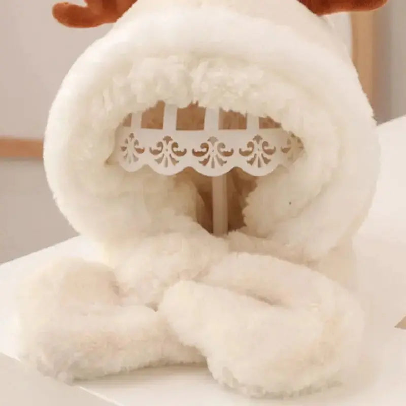 Cagoule bébé fille en fausse fourrure blanche avec des cornes de cerf marron sur le dessus. Elle est posée sur un mannequin en intérieur, à côté d’une table en bois clair.