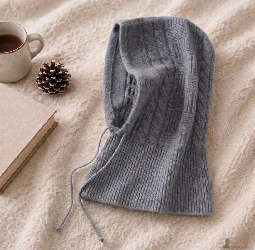 Cagoule en cachemire pour femme grise posée sur plaid avec détail du tricot et ouverture visage - Espace Cagoules