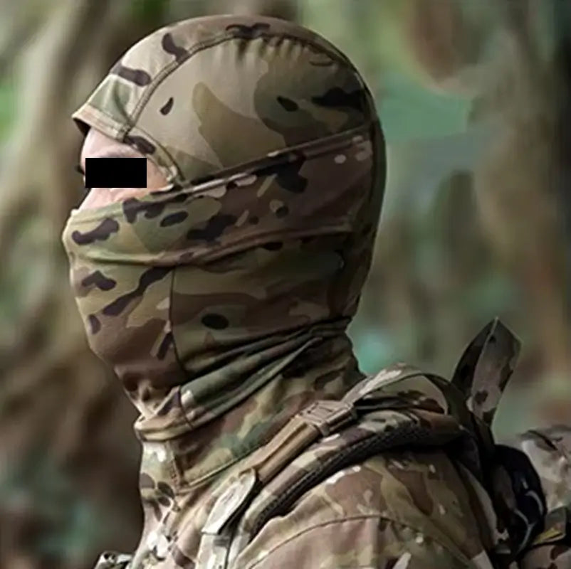 Military camouflage balaclava in forest pattern worn by a soldier, equipped with a tactical backpack, in a wooded environment.