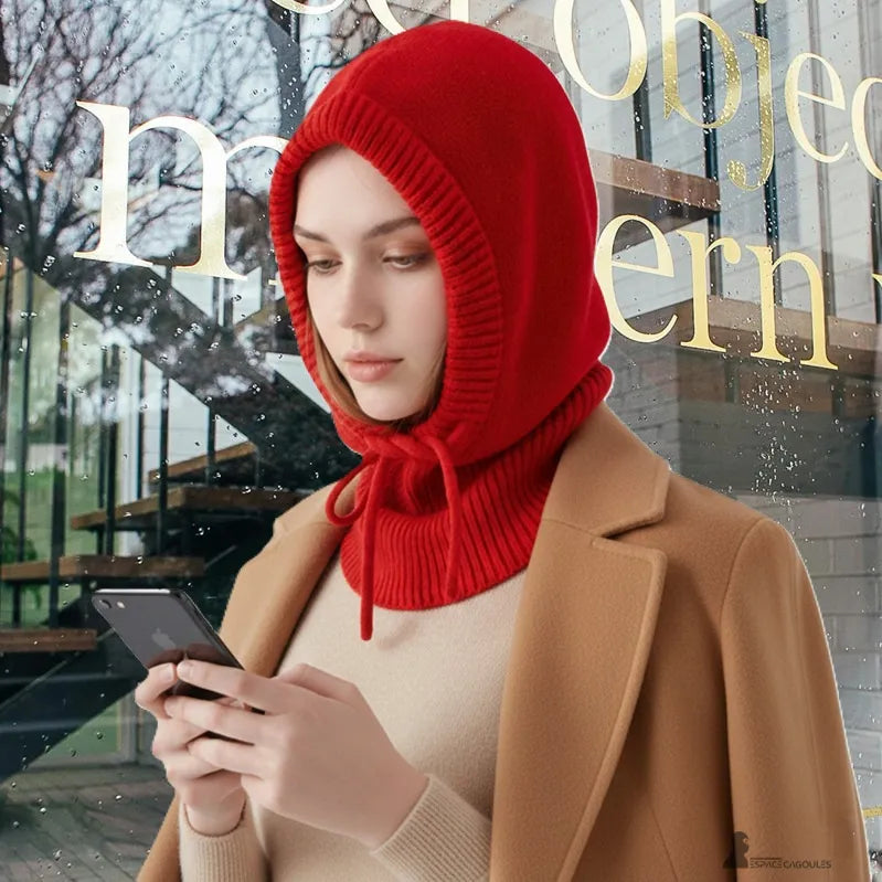 Passamontagna con cappuccio donna rossa indossata all'esterno, donna concentrata sul suo telefono davanti a una vetrina bagnata dalla pioggia - Spazio Passamontagna