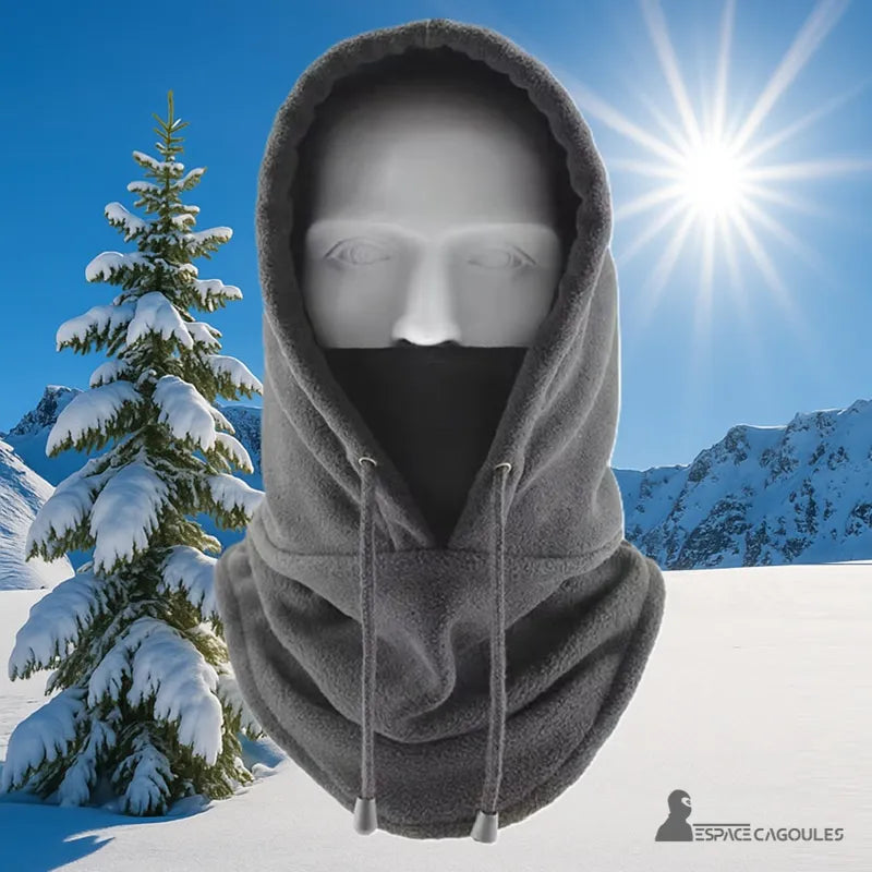 Balaclava Grey hood worn outdoors under the mountain sun, with snowy background and fir tree, ideal for winter sports.