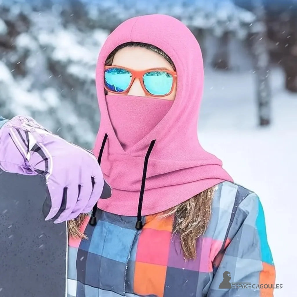 Cagoule Capuche Rose portée en situation de sport d’hiver, avec combinaison colorée et lunettes de ski dans un décor enneigé