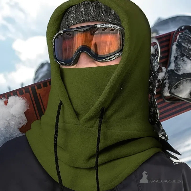 Cagoule Capuche Verte portée par un skieur avec snowboard, bonnet et masque de ski, dans un environnement enneigé.