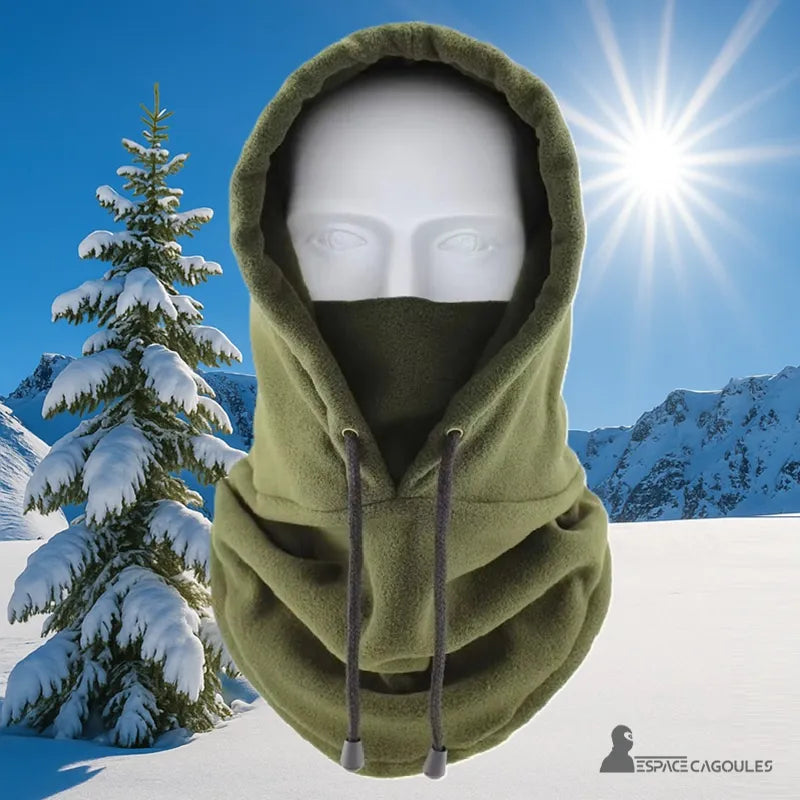 Cagoule Capuche Verte portée sur mannequin dans un décor de montagne enneigée avec ciel bleu et soleil, idéale pour l’hiver.