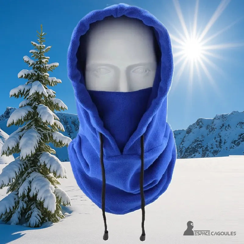 Cagoule Capuche bleue portée sur mannequin avec fond enneigé et sapin, ciel bleu et soleil, idéale pour le ski ou la randonnée.