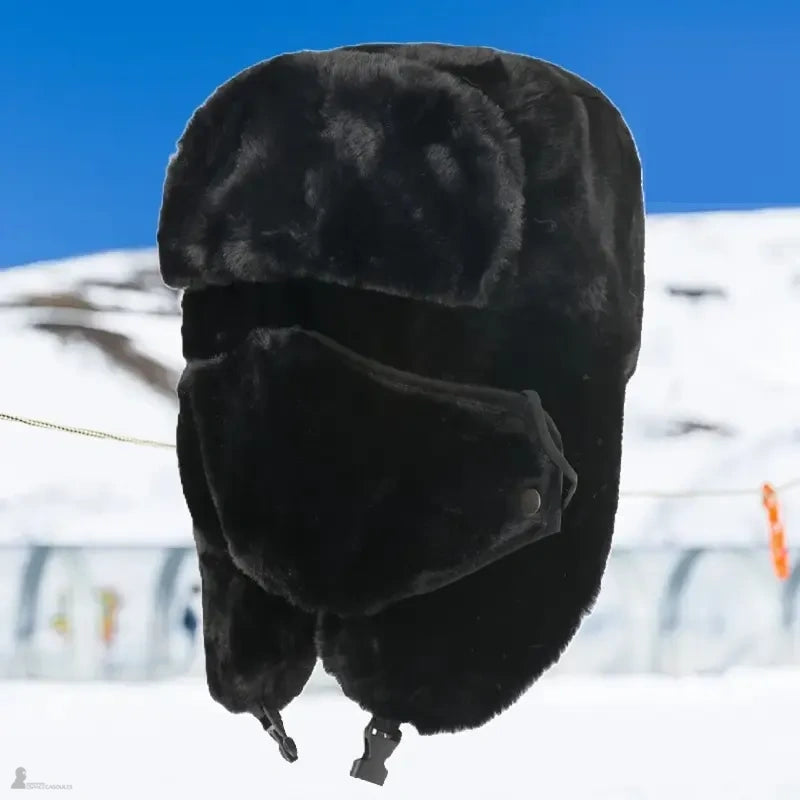 Cagoule chapka noire en fourrure avec masque facial et cache-oreilles, présentée devant un décor de piste enneigée - Espace Cagoules