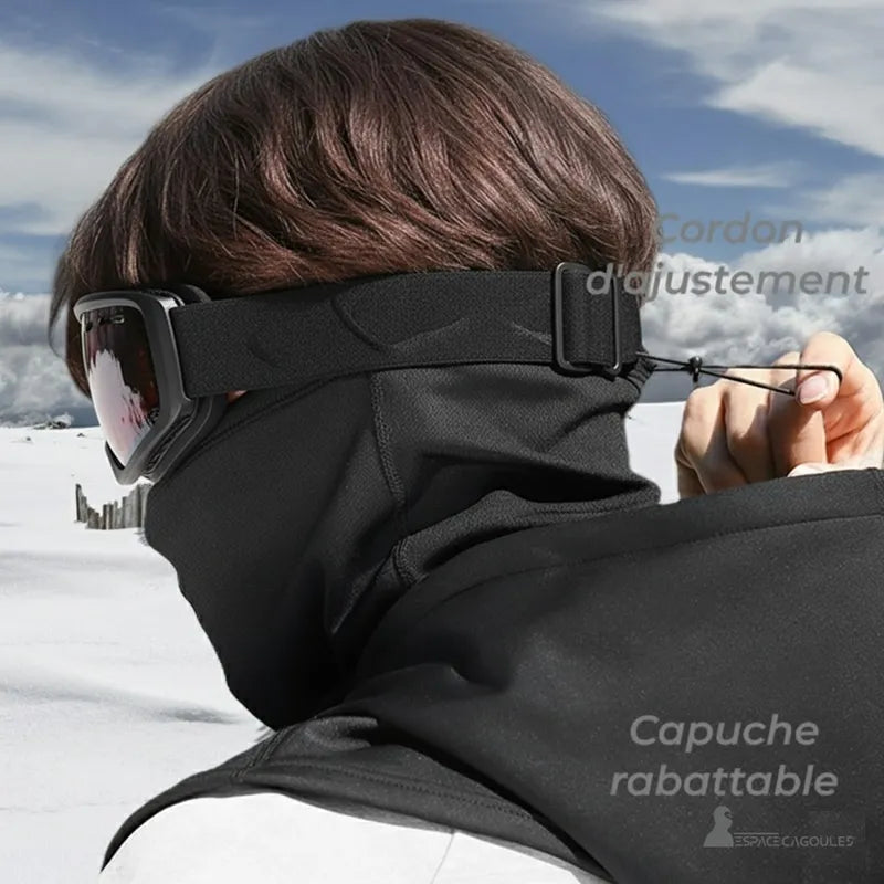 Cagoule chauffante portée par une personne avec lunettes de ski, vue arrière montrant la capuche rabattable et le cordon d’ajustement à l’arrière de la tête en environnement enneigé - Espace Cagoules