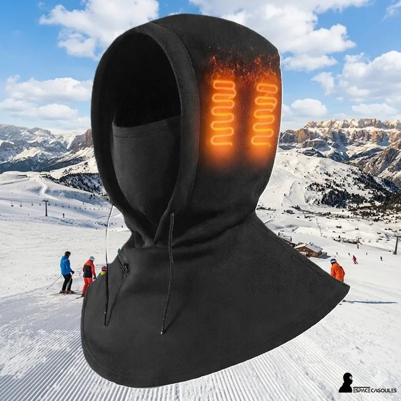 Cagoule chauffante noire avec capuche et résistances chauffantes orange visibles sur le côté de la tête, présentée sur fond de station de ski enneigée avec montagnes en arrière-plan - Espace Cagoules