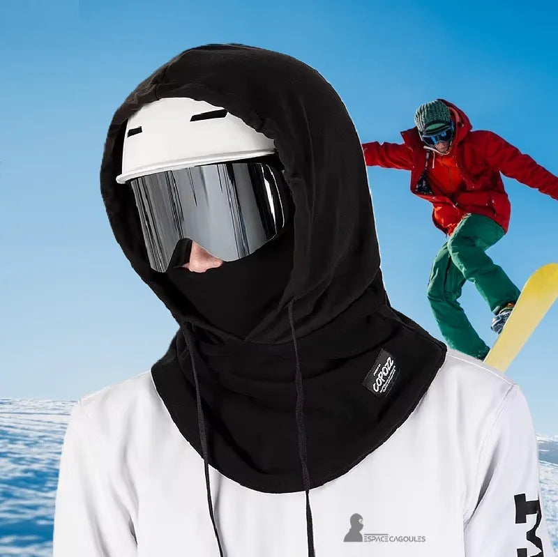 Adult Ski Hood over Helmet used in the mountains with snowboarder in the background, highlighting protection against the cold and wind during activity.
