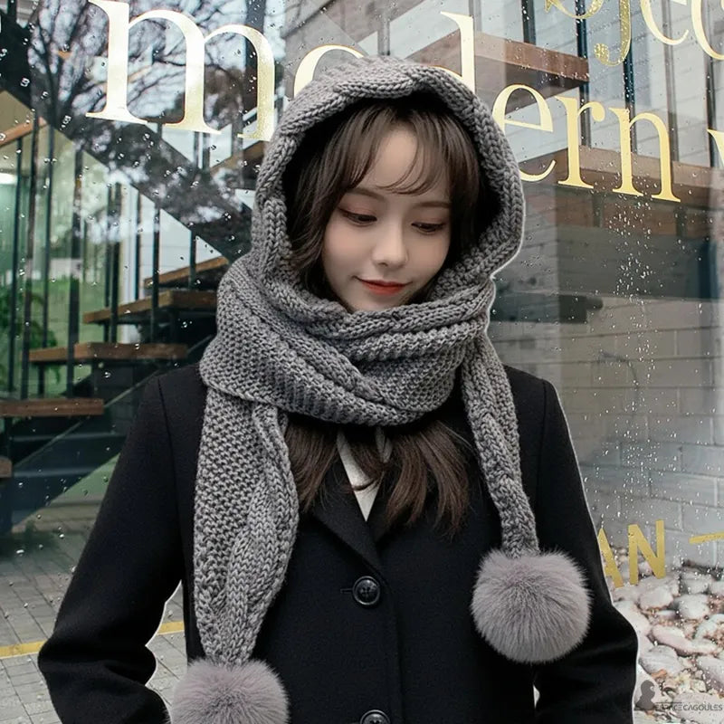 Cagoule écharpe gris clair tricotée avec pompons, femme en manteau noir devant une vitrine moderne, look d’hiver urbain – Espace Cagoules