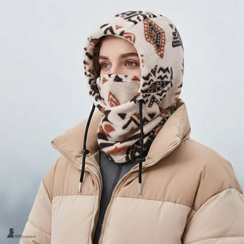 Femme en doudoune beige portant la cagoule en polaire PolarHead écru, masque relevé jusqu'au nez, paysage enneigé - Espace Cagoules