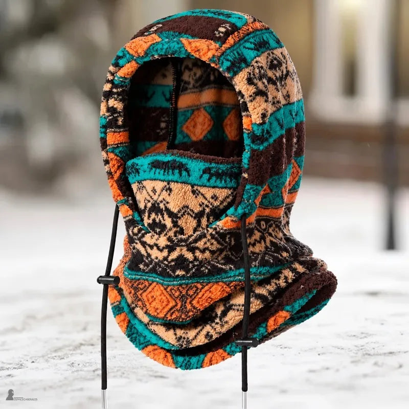 Cagoule en polaire PolarHead à motifs géométriques turquoise, orange et marron, posée sur fond de neige - Espace Cagoules