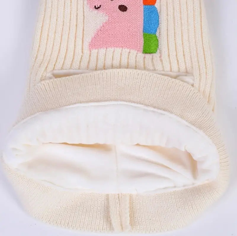 Cagoule enfant 5 ans en tricot blanc cassé avec pompons moelleux, motif de licorne colorée et doublure intérieure épaisse pour une protection optimale contre le froid.