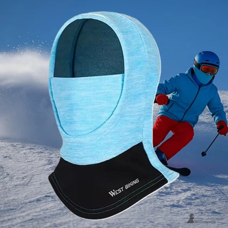 Blå barnbalaklava som bärs i backen av en ung skidåkare klädd i en blå och röd jumpsuit, som ger värme och andningsbart skydd – Espace Cagoules