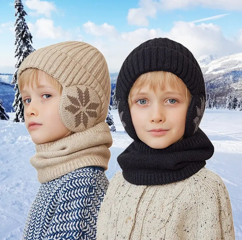 Deux enfants portant des cagoules en tricot avec cache-oreilles dans un paysage enneigé. L'enfant à gauche porte une cagoule beige avec un motif flocon, et celui à droite une cagoule noire assortie. Accessoires parfaits pour l'hiver.