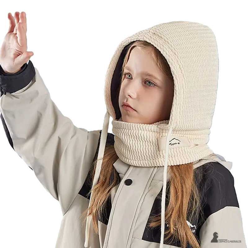 Cagoule enfant hiver avec tour de cou beige portée par une fille vêtue d'une veste de ski, capuche tricot relevée protégeant tête et nuque