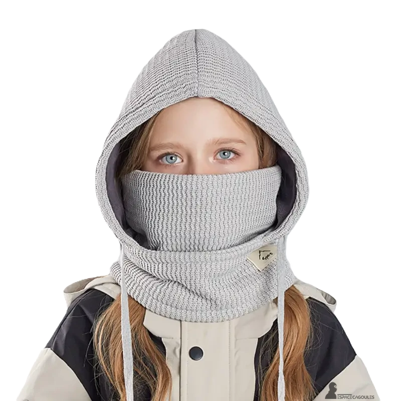 Cagoule enfant hiver avec tour de cou gris clair portée par une fille vêtue d'une veste de ski beige et noire sur fond blanc