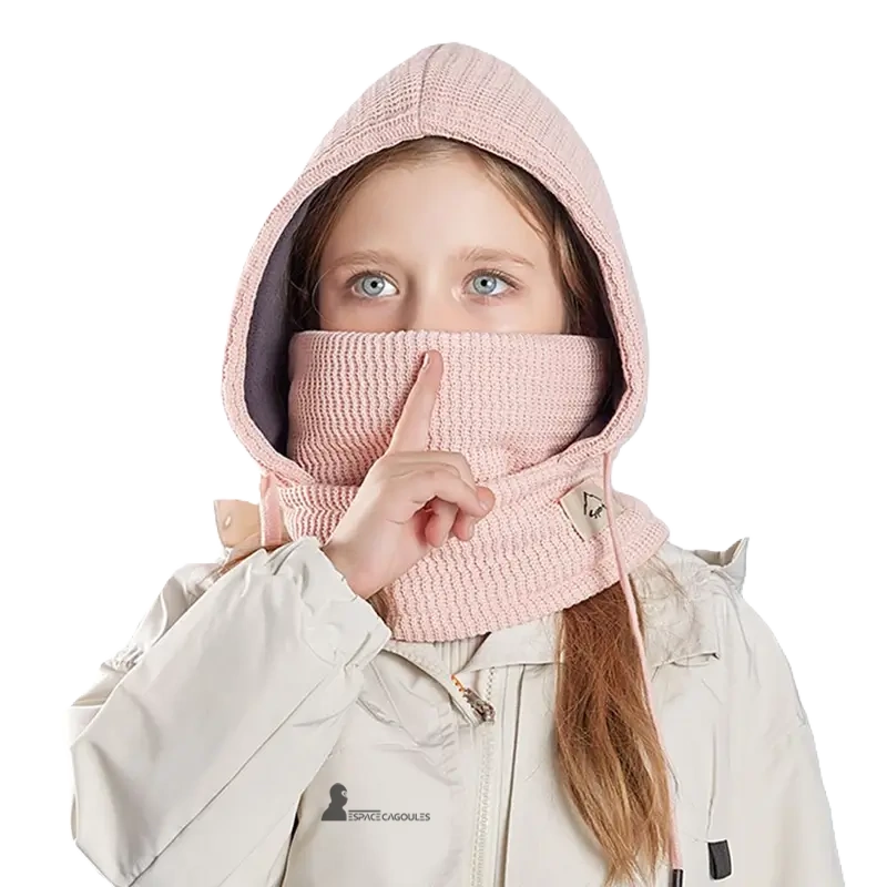 Cagoule enfant hiver avec tour de cou rose pastel portée par une fille en manteau clair capuche tricot couvrant le visage