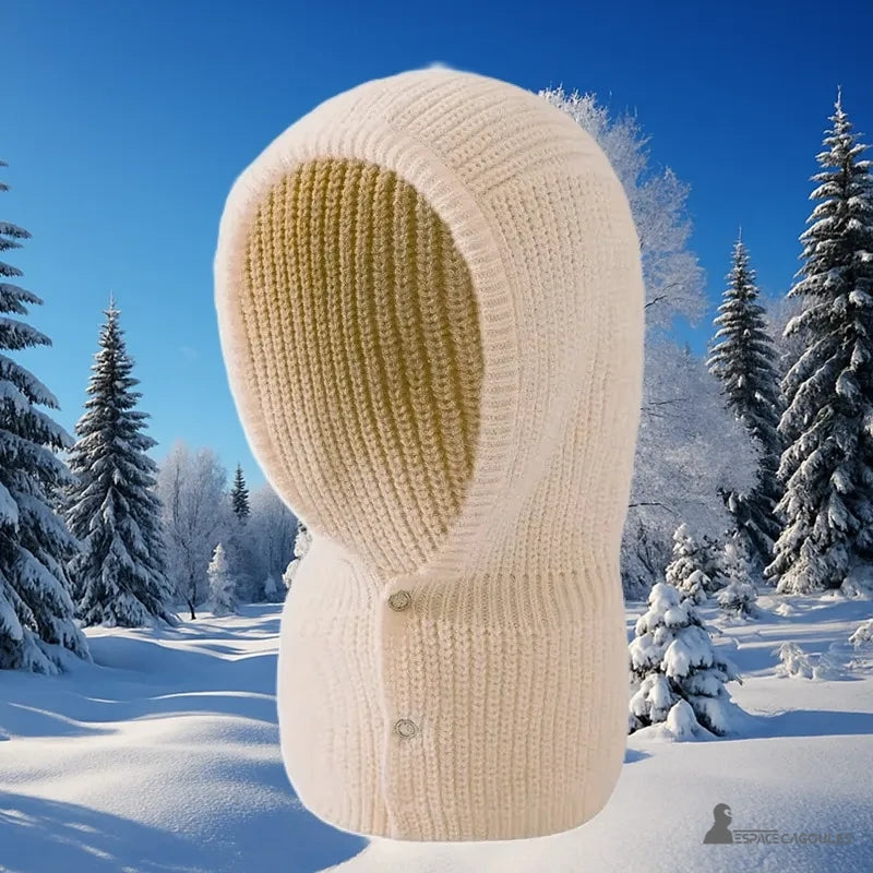 Cagoule Femme Beige en maille épaisse exposée sur fond de paysage enneigé avec sapins givrés, parfaite pour l’hiver