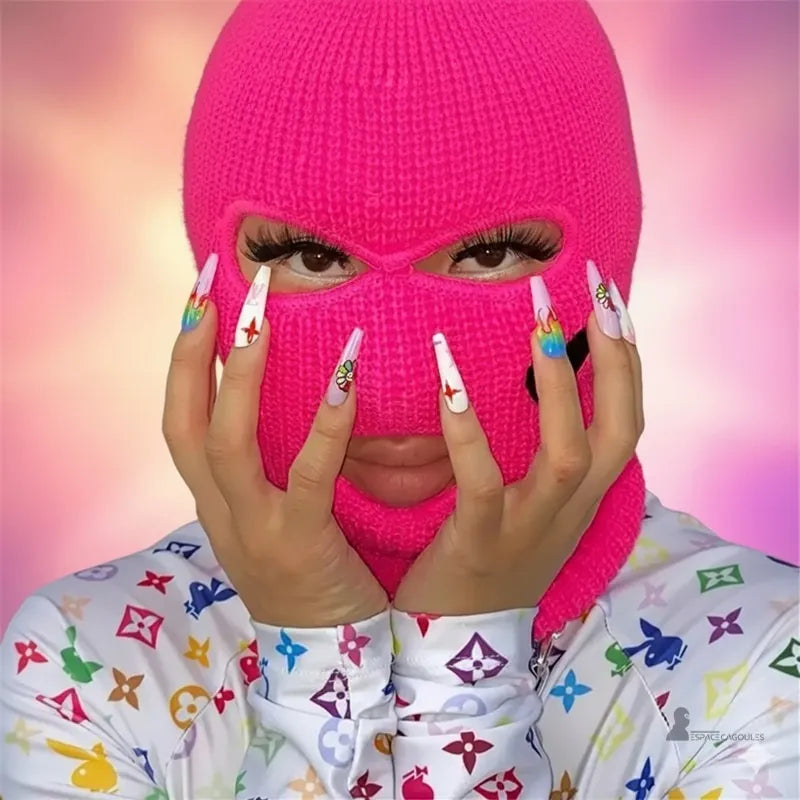 Cagoule femme fluo rose portée par une femme avec ongles décorés colorés, arrière-plan flou rose et violet