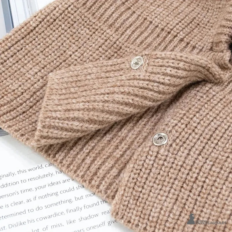 Cagoule Femme Maille beige photographiée à plat sur un fond blanc avec un magazine, montrant les boutons pression ouverts