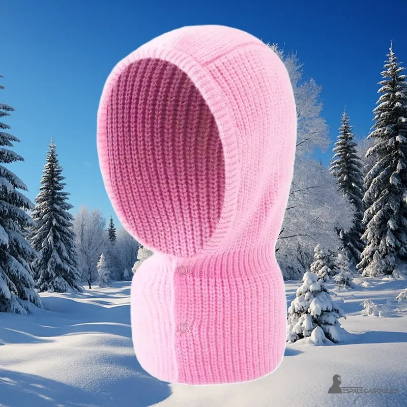 Cagoule Femme Rose en maille épaisse mise en scène sur fond de forêt enneigée, idéale pour affronter le froid hivernal