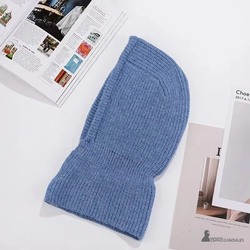 Trendige Damen-Sturmhaube aus blauer Wolle, flach auf weißem Hintergrund mit Zeitschriften gelegt, die ihren umhüllenden Schnitt zur Geltung bringen