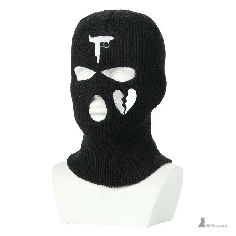 Passamontagna nero da gangster in maglia spessa con motivo di pistola e cuore spezzato bianco, mostrata su un manichino bianco a busta in studio